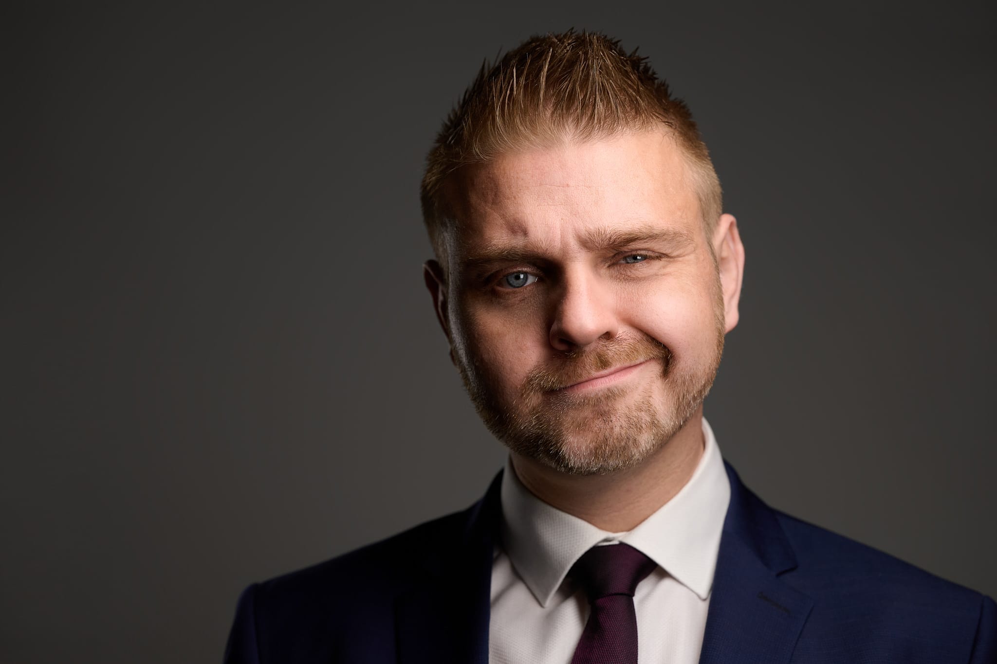 Businessporträt von Alexander Reith im Anzug mit skeptischem Blick vor grauem Hintergrund